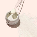 A small metal tin of Manucurist's Golden Glazed Effect Powder—fine, off-white powder that gives nails a pearly gold shimmer—sits centered on a light beige background, casting a soft left shadow.