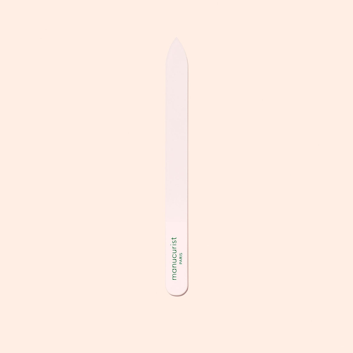 The Manucurist-us Glass Nail File features a pointed tip and "manucurist" in green near the base, shown vertically on a pale beige background.
