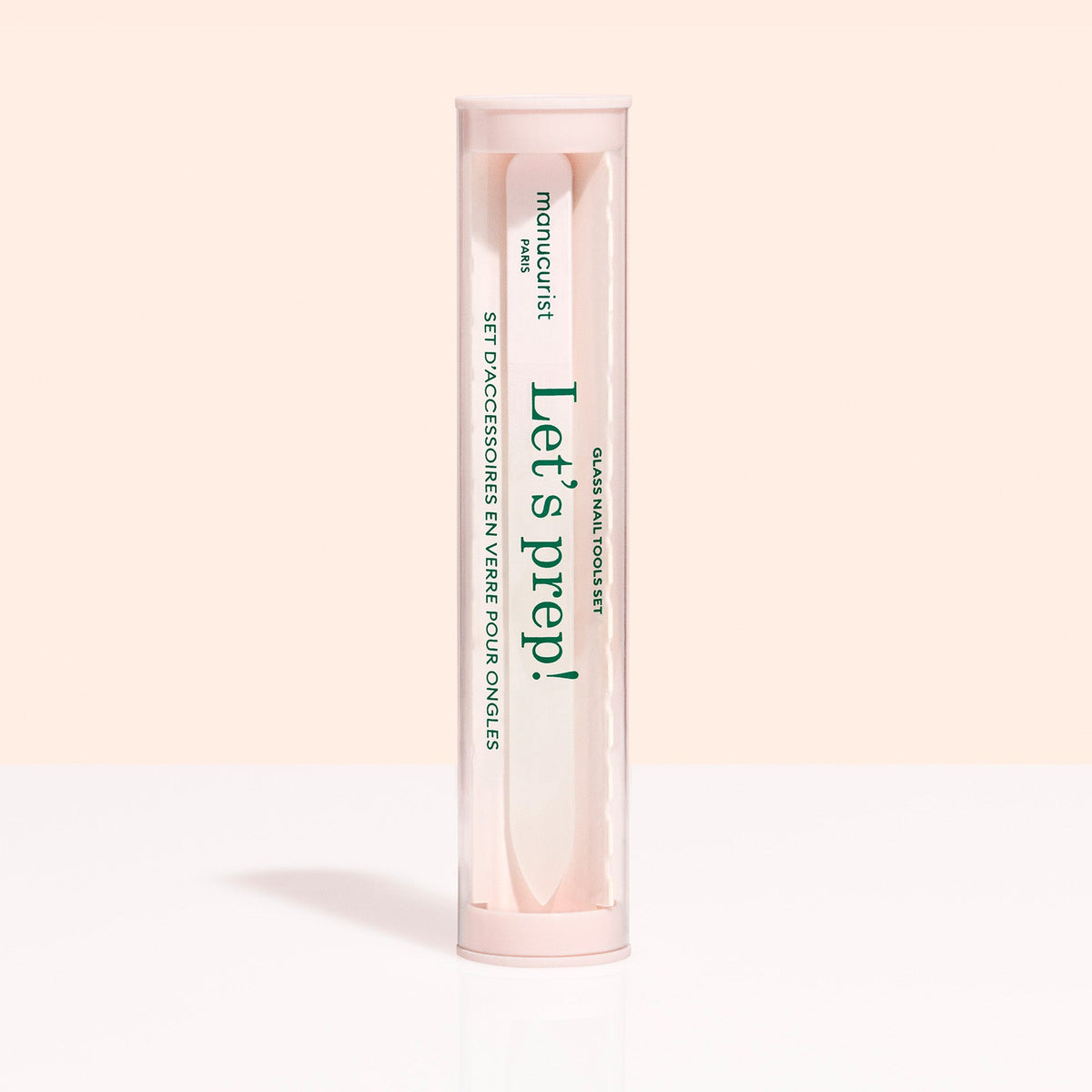 A cylindrical Lets prep! case holds the Manucurist-us Glass nail accessory trio, including a glass cuticle pusher and nail file, shown on a light beige background.