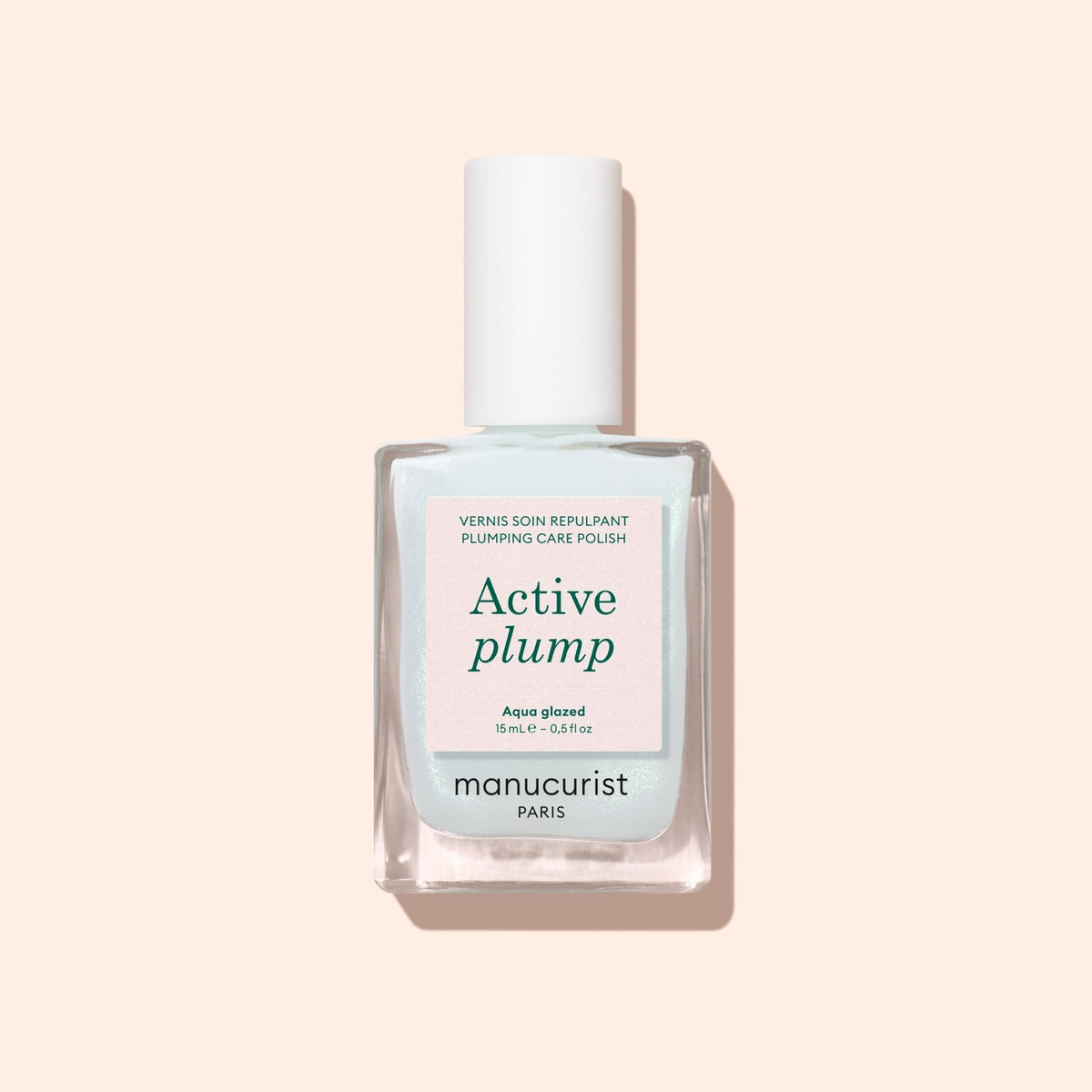 A bottle of Manucurist Active™ Plump Aqua Glazed plumping care polish with a white cap is displayed against a pale pink background. This volumizing nail care formula, featuring collagen nail polish, presents its label text on the front of the clear bottle.