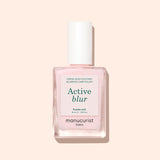 A bottle of Manucurist Active™ Blur nail polish in powder pink, showcasing a flawless matte finish and topped with a white cap adorned with a minimalist label, displayed against a light beige background.