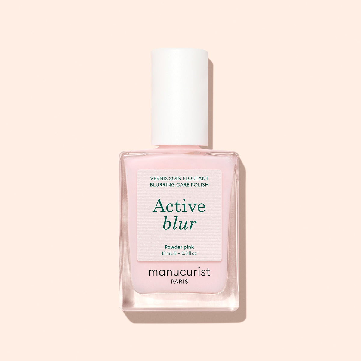A bottle of Manucurist Active™ Blur nail polish in powder pink, showcasing a flawless matte finish and topped with a white cap adorned with a minimalist label, displayed against a light beige background.