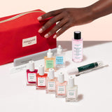 The Manucurist Super Ultimate Active Manicure Kit is a comprehensive nail care set featuring manicure tools and products for healthy nails, including nail files, cuticle remover, six bottles of nail polish, three nourishing care oils, remover, and a stylish red manicurist pouch—all neatly arranged on a beige background.