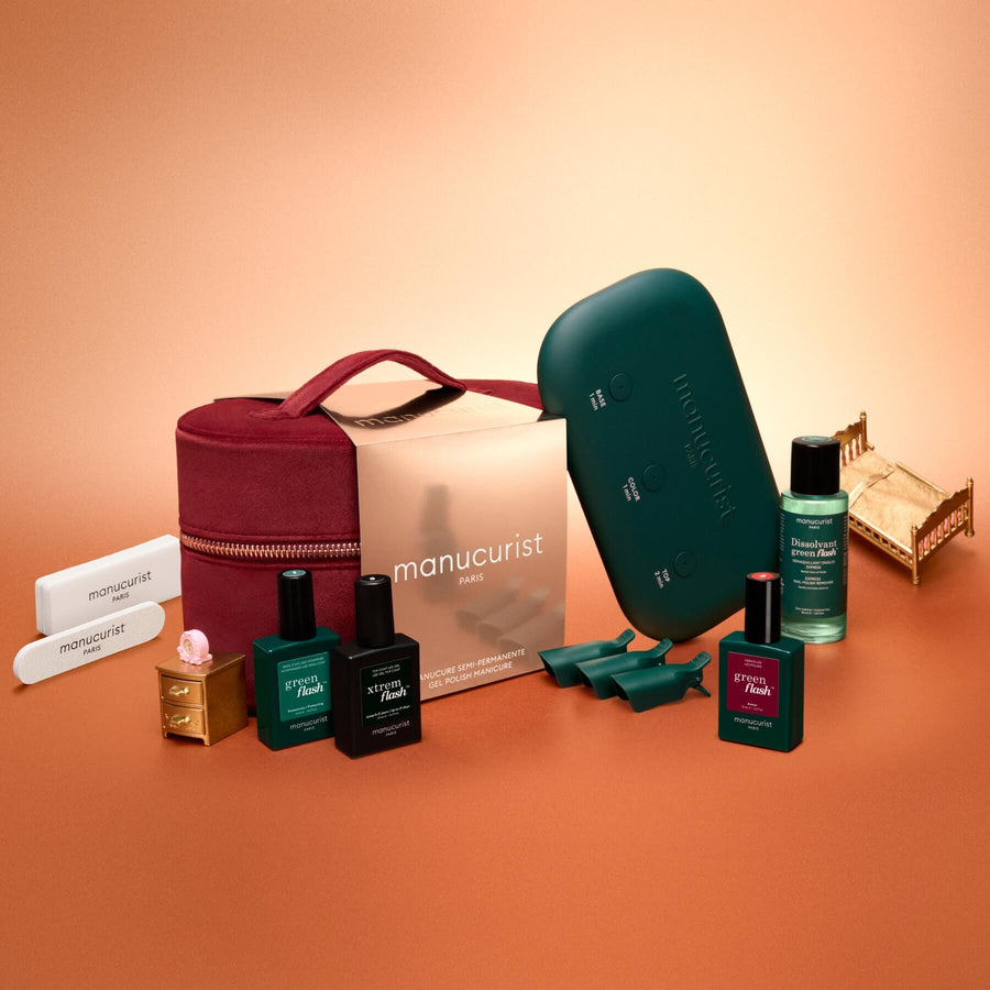 The Manucurist Green Flash™ Discovery Kit Gift Set, featuring a stylish red velvet case, teal lamp, gel nail polishes, essential nail care products, files, and cuticle tools arranged neatly on an orange background—everything you need for a salon-style manicure at home.