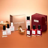 The Manucurist Green™ Starter Kit Gift Set features a pink pouch, a gold box, four bottles of naturally derived nail polish for a gel effect manicure, and three nail care bottles, all elegantly arranged on a peach-colored background.