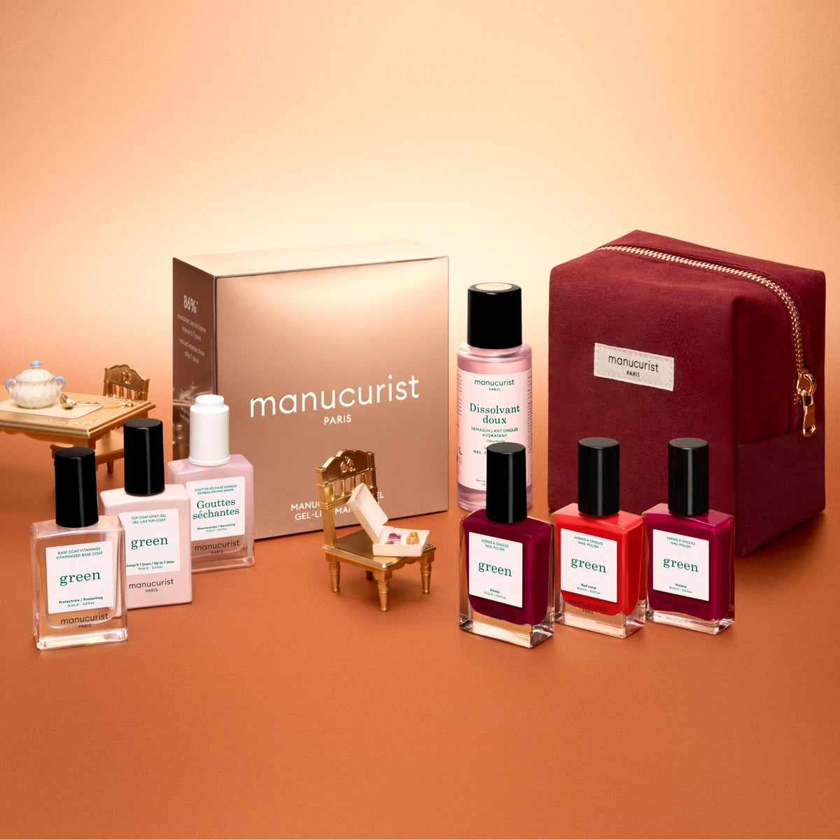 The Manucurist Green™ Starter Kit Gift Set features a pink pouch, a gold box, four bottles of naturally derived nail polish for a gel effect manicure, and three nail care bottles, all elegantly arranged on a peach-colored background.