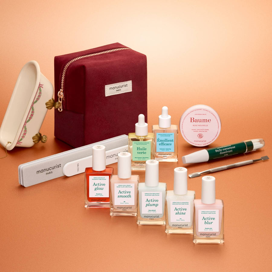 The Manucurist Active™ Super Ultimate Gift Set is perfect for your active manicure routine, featuring files, a cuticle tool, nail polishes, gentle nail remover, cuticle oils, balm, and a red velvet pouch—all arranged neatly on a peach-colored background. Ideal as a thoughtful holiday gift.