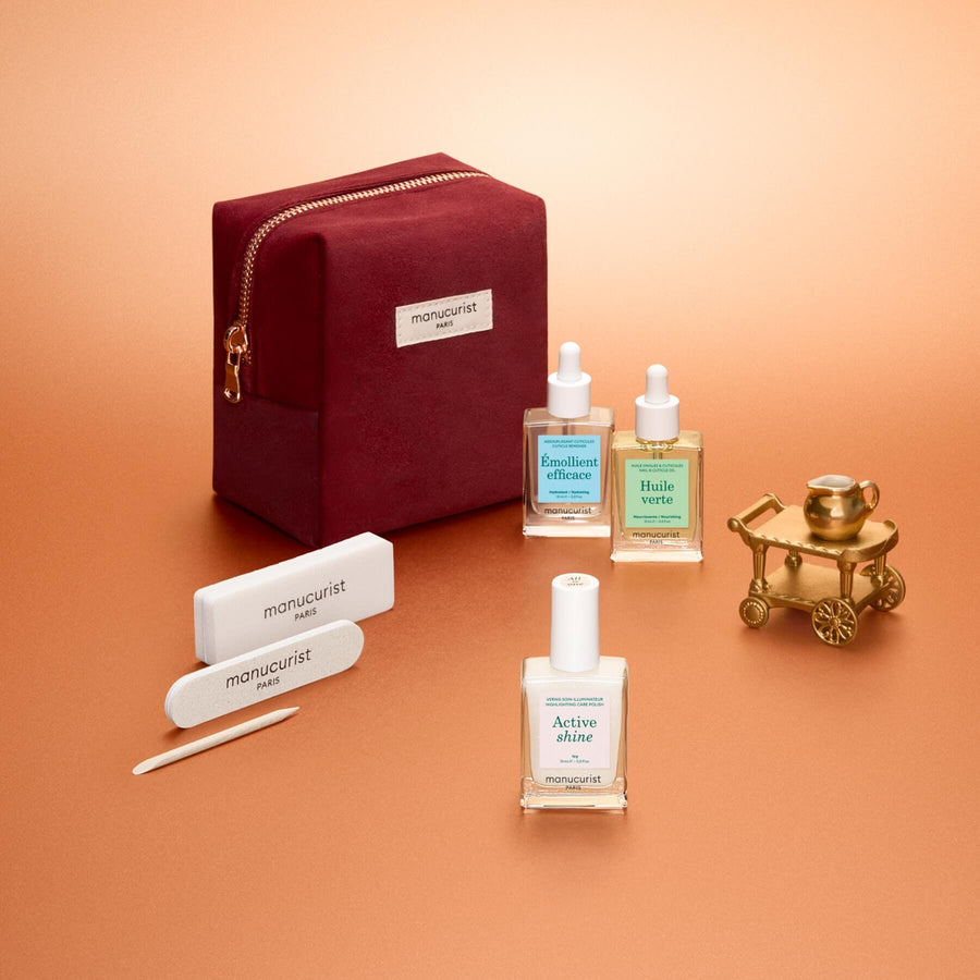 The Manucurist Active™ Discovery Gift Set is beautifully displayed on a peach background and features a red velvet pouch, nail files, cuticle pusher, two bottles of nail care oil, and a bottle of nail serum—all perfectly arranged. This set makes an ideal holiday gift for anyone who loves a relaxing manicure routine and gorgeous nails.