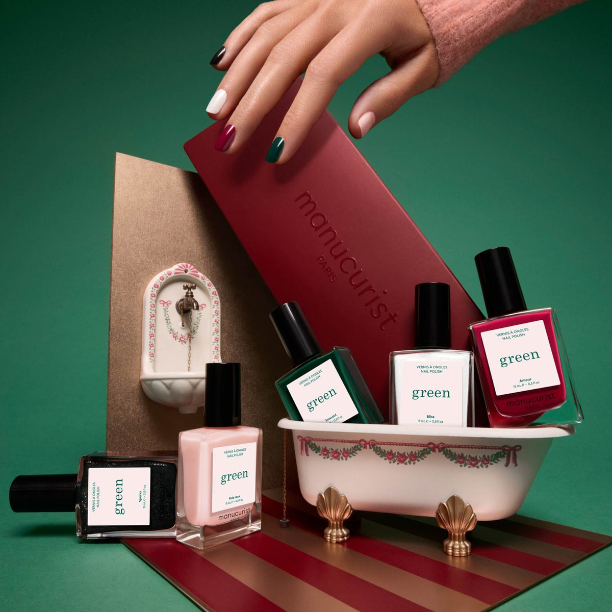 Five horizontal swatches of Manucurist’s Customizable 5-pack gel nail polish, labeled Amour (red), Emerald (green), Bliss (white), Pale Rose (pink), and Sparks (black with glitter), each shown as a brushstroke to highlight the color. These shades pair perfectly with our Green Flash gel polish collection and can be easily removed with an acetone-free nail polish remover.