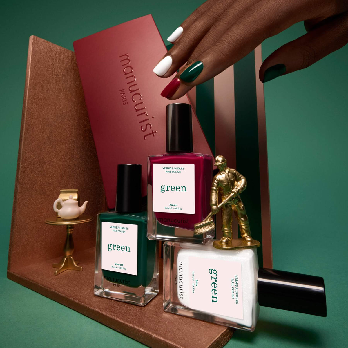 Three horizontal sections display close-ups of Manucurist Green Flash gel polishes from the Customizable Trio: a deep red shade labeled Amour, a dark green labeled Emerald, and a shimmery white labeled Bliss. Each section showcases a streak of glossy Green Flash gel polish, highlighting vibrant color payoff and shine—all easily removed with your favorite nail polish remover.