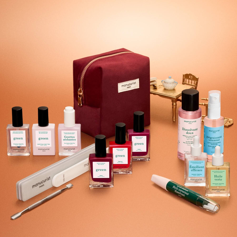 Flat lay of the Manucurist Green™ Starter Kit Gift Set, showcasing manicure essentials like naturally derived nail polish, two small bottles, manicure tools, a nail file, a burgundy pouch, and a gold box—all artfully arranged in neat rows and columns on a copper backdrop.