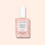 A bottle of Manucurist Active™ Shine Opal plant-based nail polish, featuring a white cap and filled with a light pink, shimmery formula designed to strengthen nails, displayed against a pale beige background.
