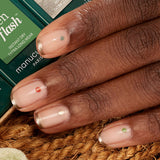 Five bottles of Manucurist's Spice Lover nail polish are displayed on a striped cloth with dried purple petals—some in a bowl. Wooden chopsticks rest nearby, and one bottle sits on a beige plate in the upper right corner.