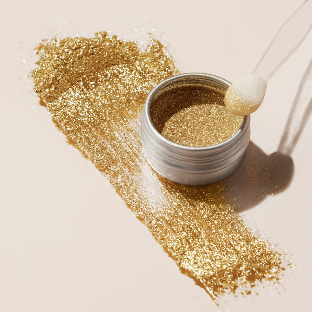 A round Manucurist Golden Chrome Powder container, viewed from above on a pale beige background, ideal for achieving a dazzling chrome finish.