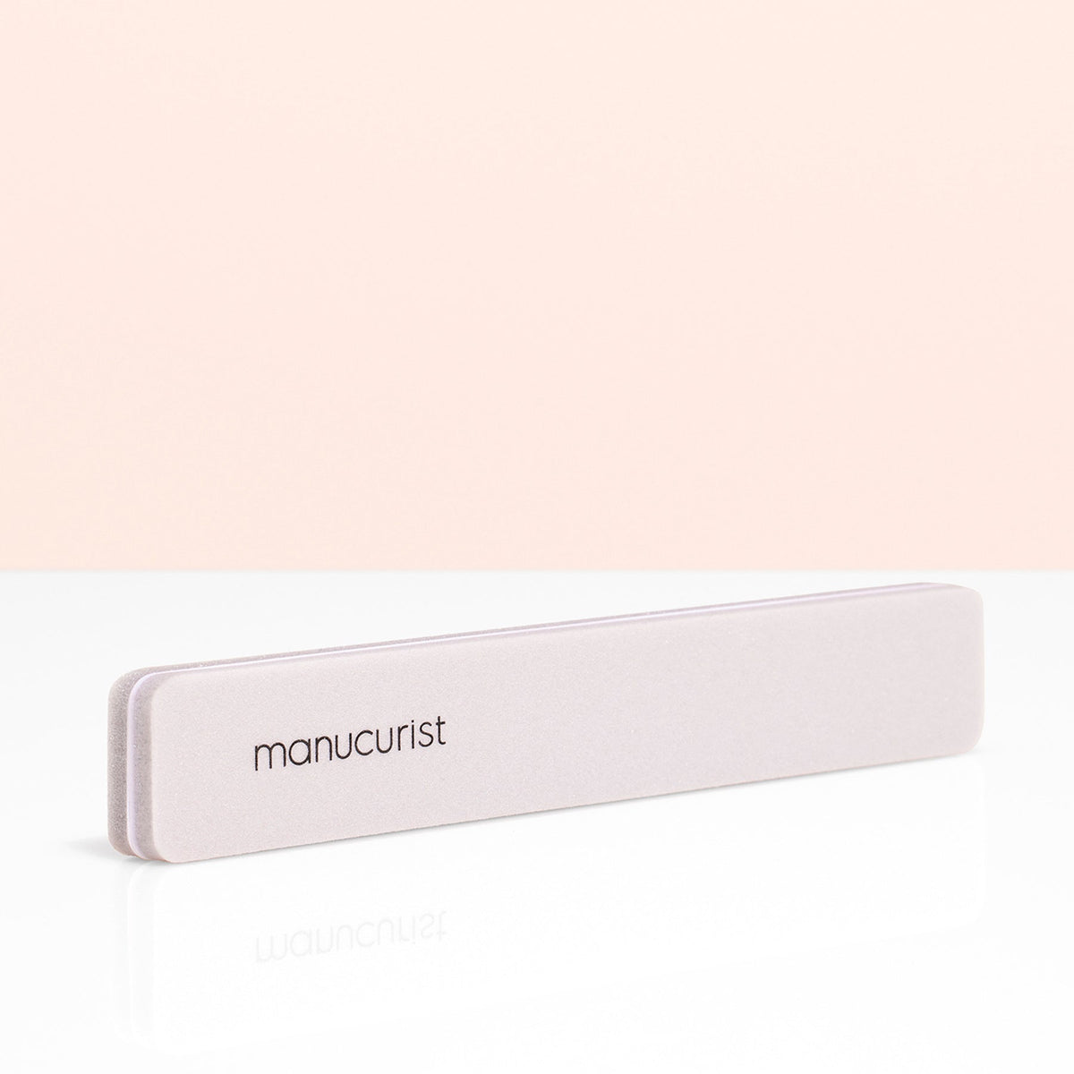 A rectangular gray Manucurist Nail buffer sponge with rounded edges is placed vertically on a light beige background, perfect for smoothing the nail plate and prepping your manicure.