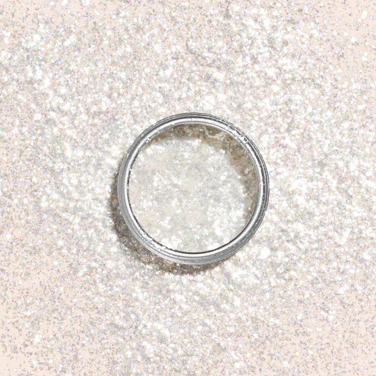 The Manucurist Pearlescent Glitter Flakes come in a small round container on a pale peach background, casting a soft shadow—ideal for adding dazzling shimmer to your next manicure.