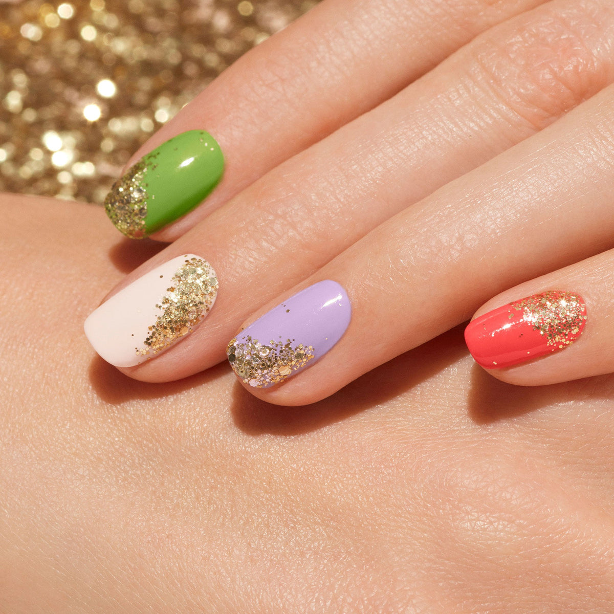 A hand selects a bottle of Manucurist Glitter in Love nail polish from a set of five in a box, with a toy fish nearby. Inset circles display nail art brushes and biodegradable glitter on a neutral background.