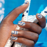 Two bottles of Manucurist Midnight Swim nail polish are shown with a wooden cuticle stick, in front of a coiled white rope with navy accents on a white background—ideal for creative nail art.