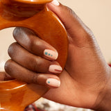 Four bottles of Manucurist Geometric Obsession nail polish in green and cream shades from the Autumn 2023 collection are displayed on a textured brown surface with yellow powder, two nail art brushes, and geometric nail art inspiration.