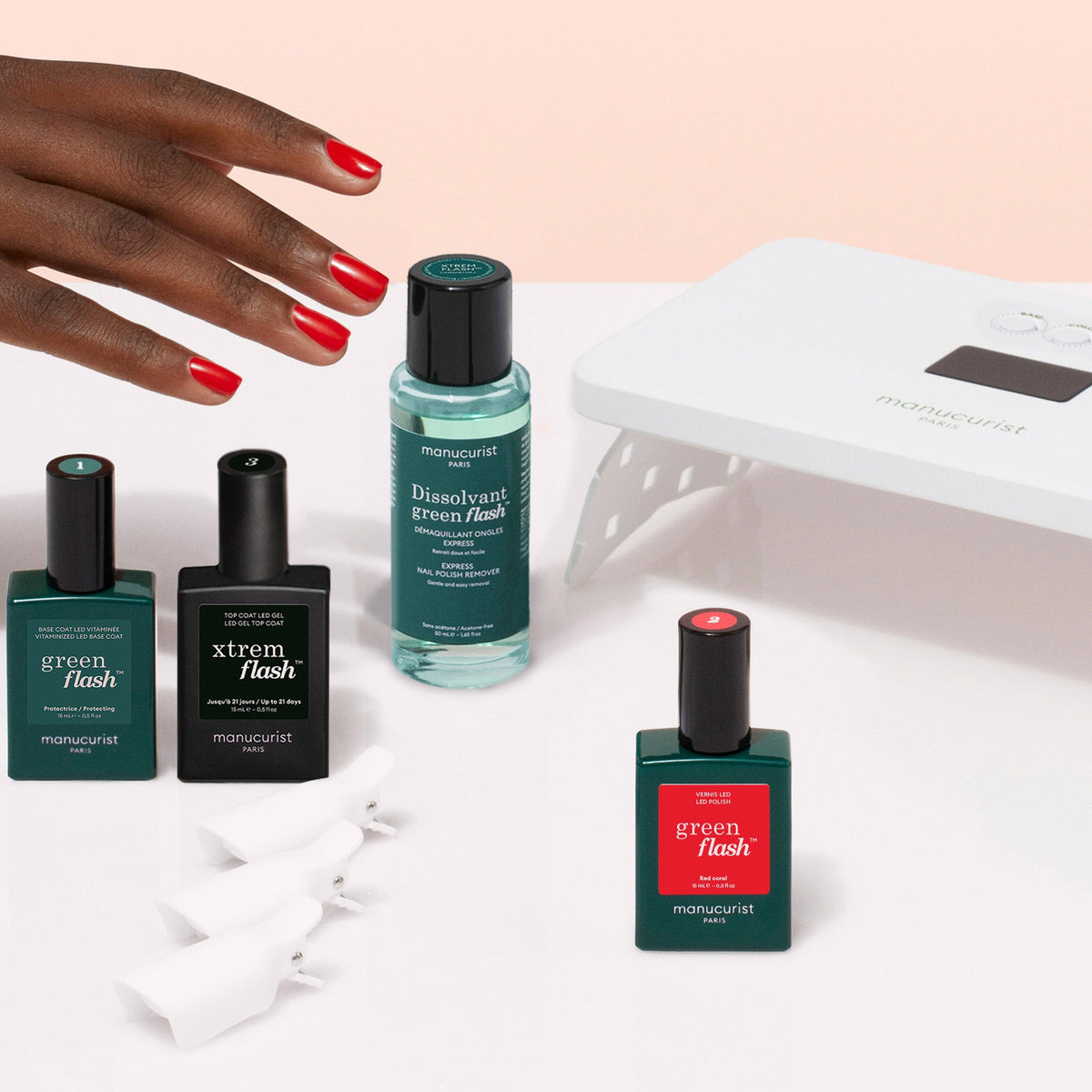 The Manucurist Discovery Kit features a white LED lamp, three nail polishes, a vitaminized base coat, remover, and four white nail clips—perfect for an ultra-glossy manicure—beautifully displayed on a light pink background.
