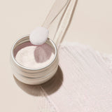A round metal container of Manucurist Pink Glazed Effect Powder, featuring a subtle pearlescent sheen, is viewed from above against a light beige background.