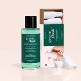 A bottle of Manucurist-us Green Flash™ Remover  Clips Duo stands beside an open box with five reusable fingertip clips, each featuring a white textured cap. The background is a soft beige color.