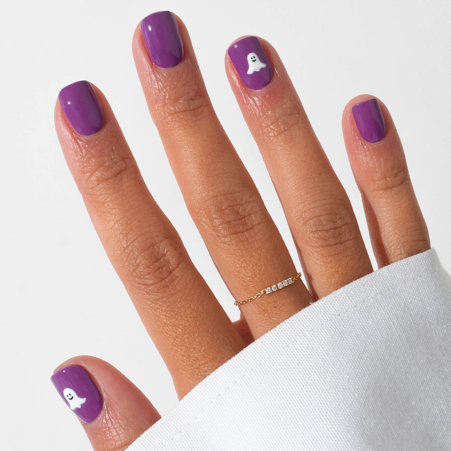 Three bottles of Manucurist’s Witchy  Wicked nail polish in purple, black, and clear, plus a pot of shimmery purple powder—perfect for Halloween nail art—are displayed on a geometric pastel background.
