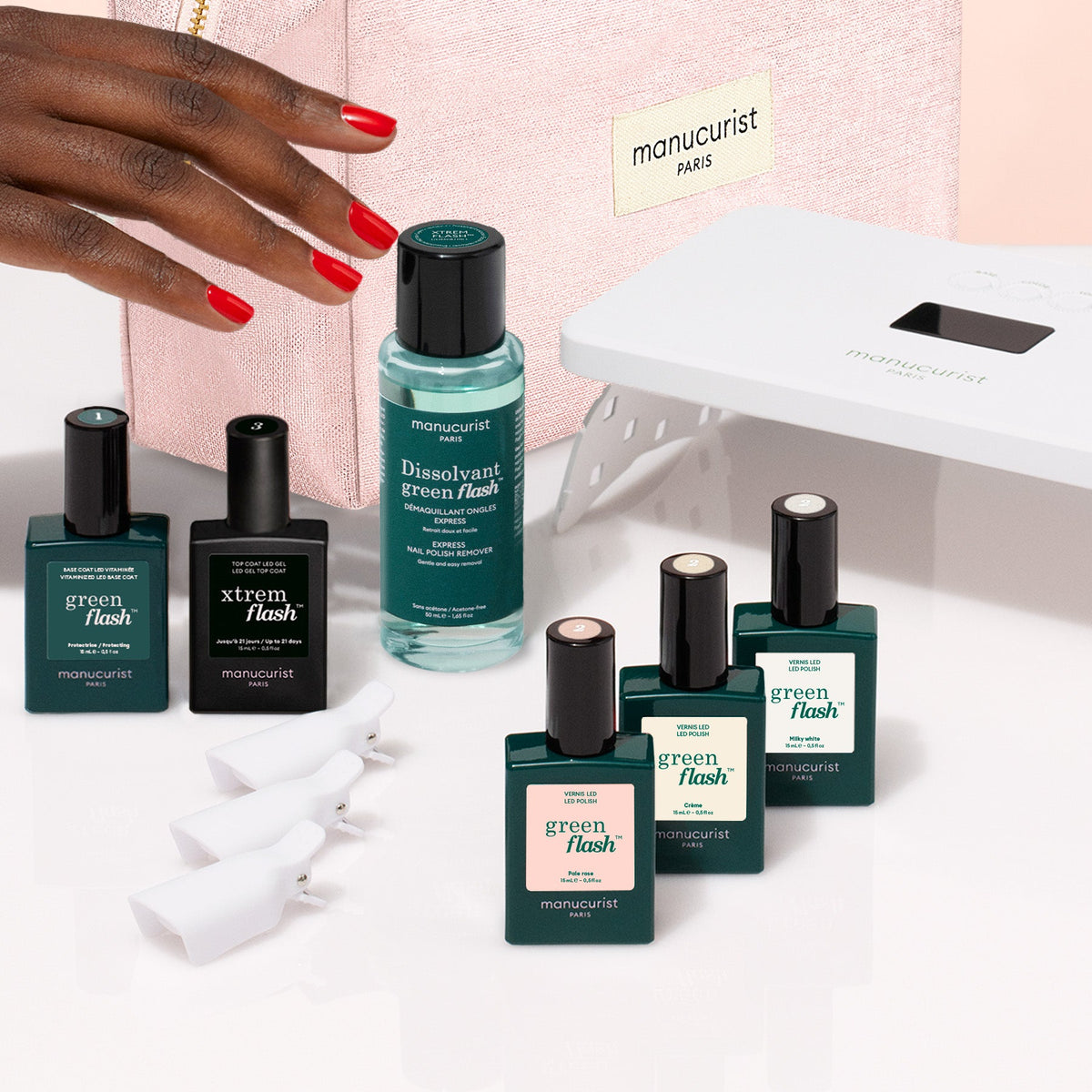 A Manucurist Starter Kit - Soap Nails LED Gel Polish including a white LED lamp, nail polish remover, five colored polishes, a top coat, and five finger clips, arranged next to a zippered makeup bag.