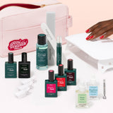 The Manucurist Ultimate Kit features a pink pouch, gel polishes, nail files, a cuticle pusher, LED lamp, remover bottles, and more—everything you need for an ultra-glossy manicure on a light beige background.