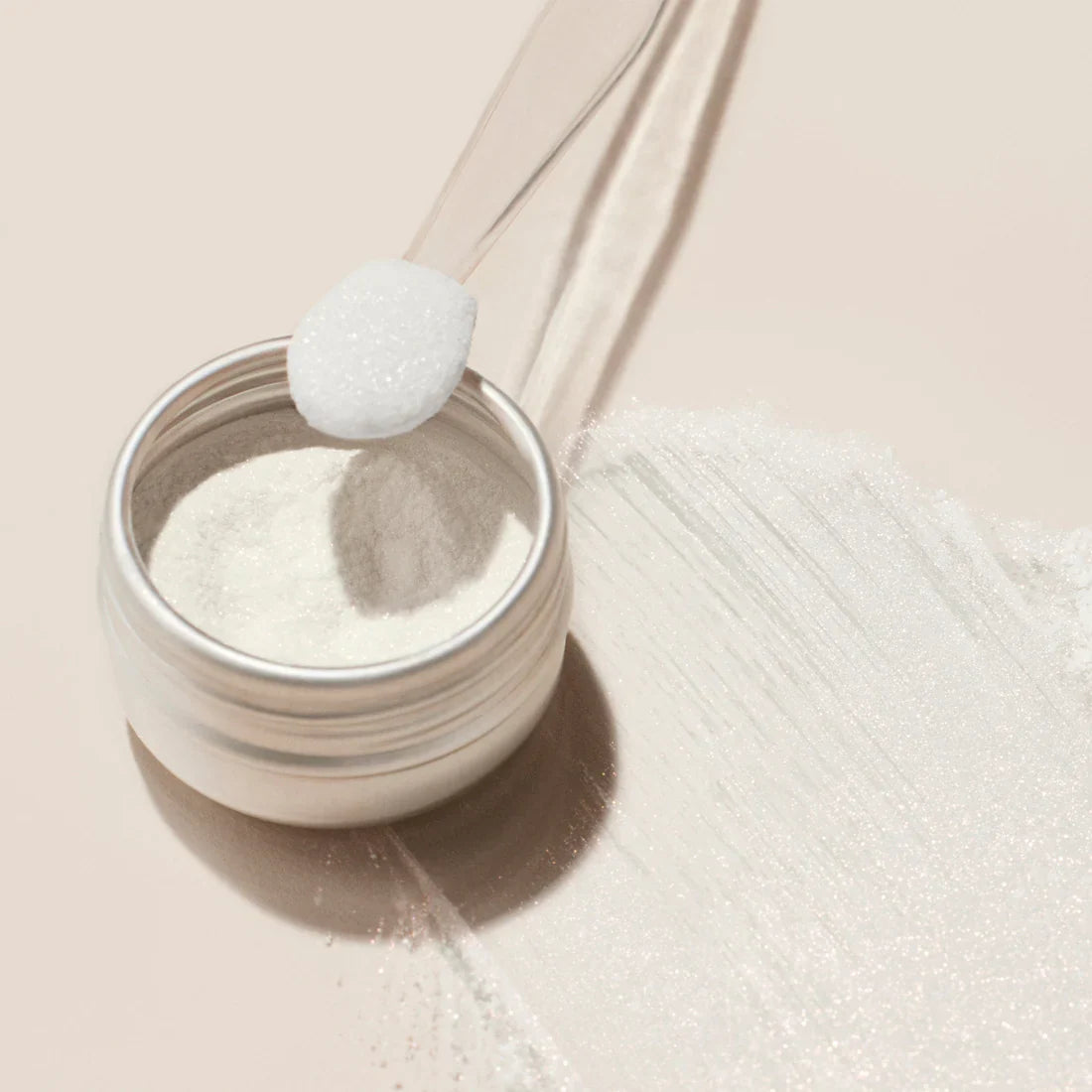 The Manucurist White Glazed Effect Powder, a fine shimmery white powder in a small round metal tin, is displayed against a pale beige background with a soft shadow to the left—ideal for creating glazed nail looks.