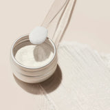 The Manucurist White Glazed Effect Powder, a fine shimmery white powder in a small round metal tin, is displayed against a pale beige background with a soft shadow to the left—ideal for creating glazed nail looks.