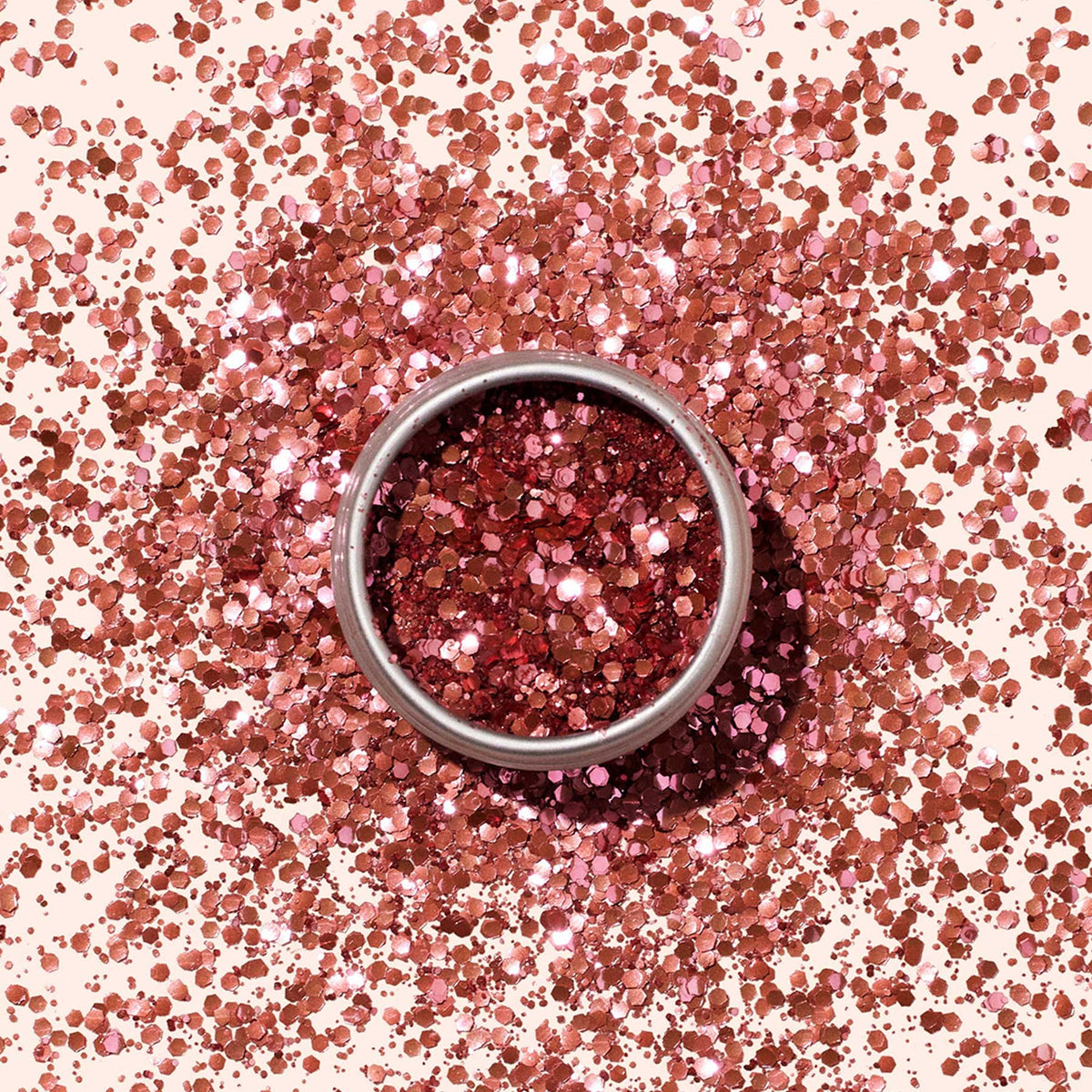 A small round container of Manucurist Pink Quartz Biodegradable Glitter, filled with shiny, chunky rose gold pieces, sits on a light beige background—perfect for adding eco-friendly sparkle to your nail art.