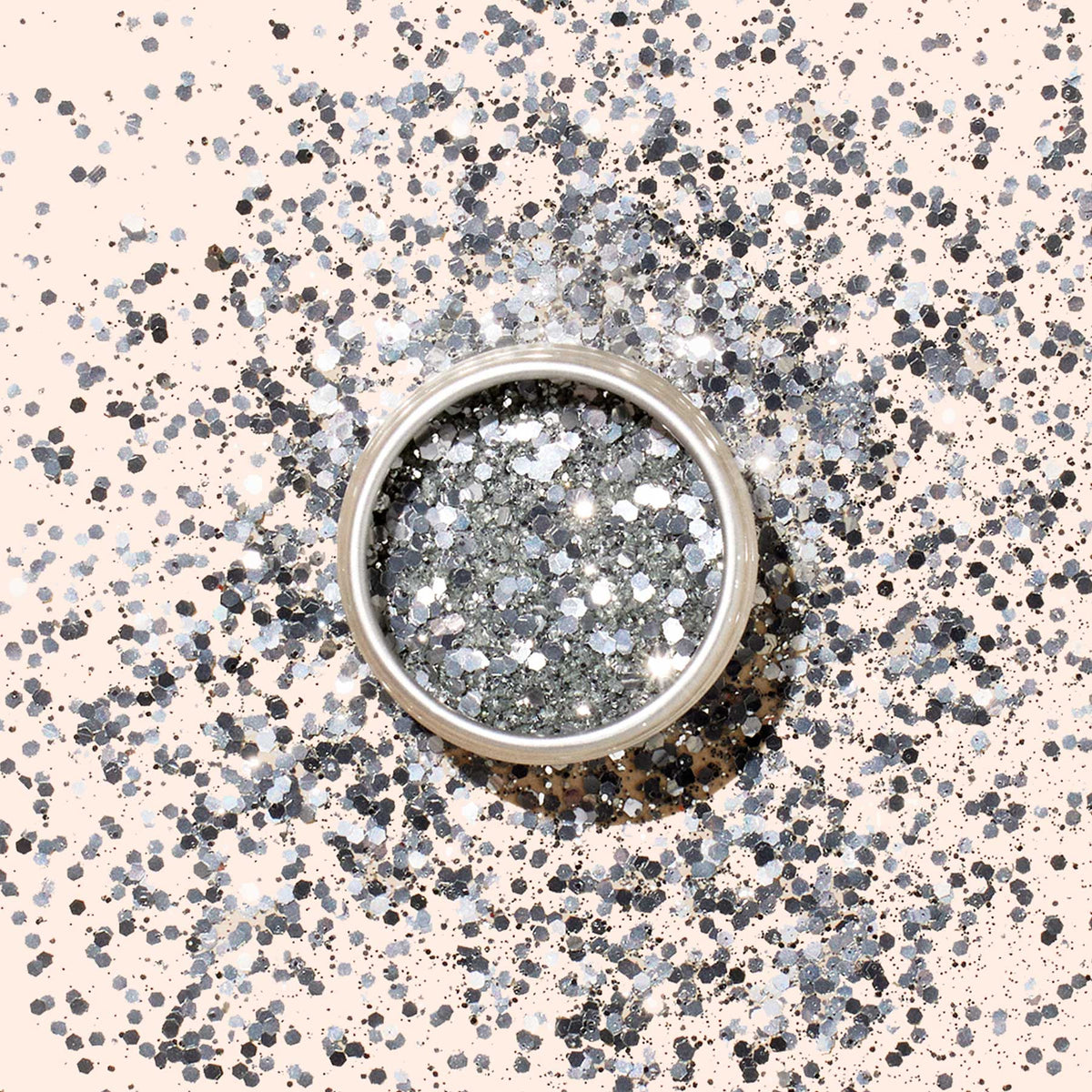 A round container of Manucurist Silver Biodegradable Glitter, designed for nail art, rests on a light beige background with a soft shadow cast to the left.