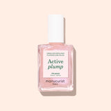 A bottle of Manucurist Active™ Plump Pink Glazed collagen nail polish in a light pink shade, featuring a white cap and displayed against a pale peach background—ideal for hydrated nails and gentle, plant-based nail care.