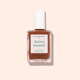 A bottle of Manucurist Active Smooth 03 nail treatment with a white cap, clear glass bottle, and beige-brown label is shown against a pale pink background.