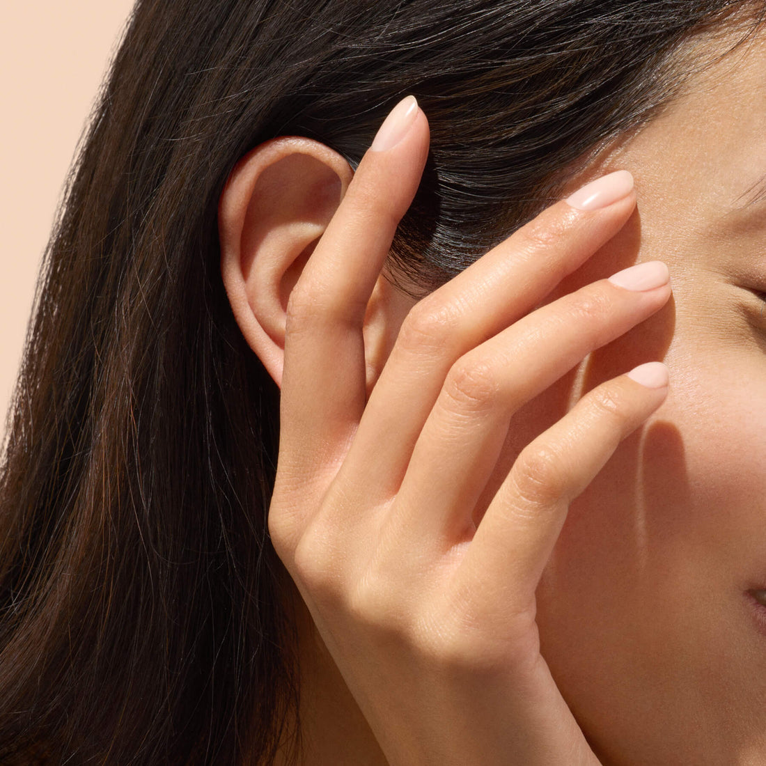 Main aux ongles nude touchant le menton